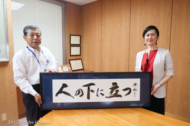 A modern glass-walled meeting room featuring a framed calligraphy of the corporate philosophy.